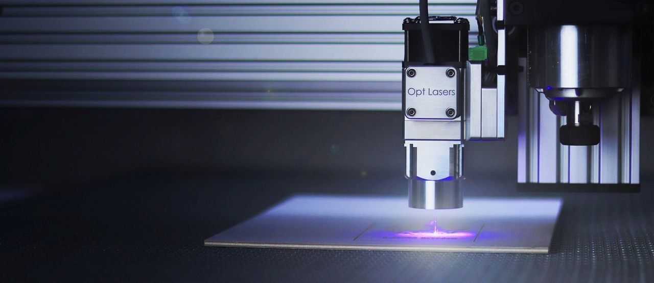 Close-up of a laser engraver working on a surface under blue lighting.